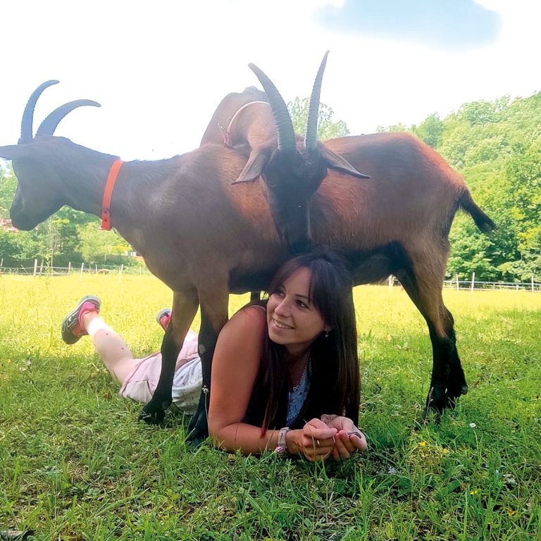 Femme allongée dans l'herbe avec deux chèvres derrière elle.