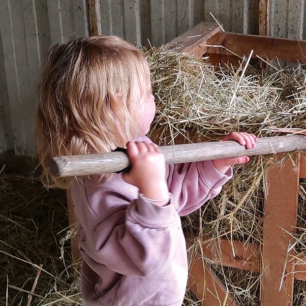 Enfant tenant une barre en bois, près de foin dans une grange.